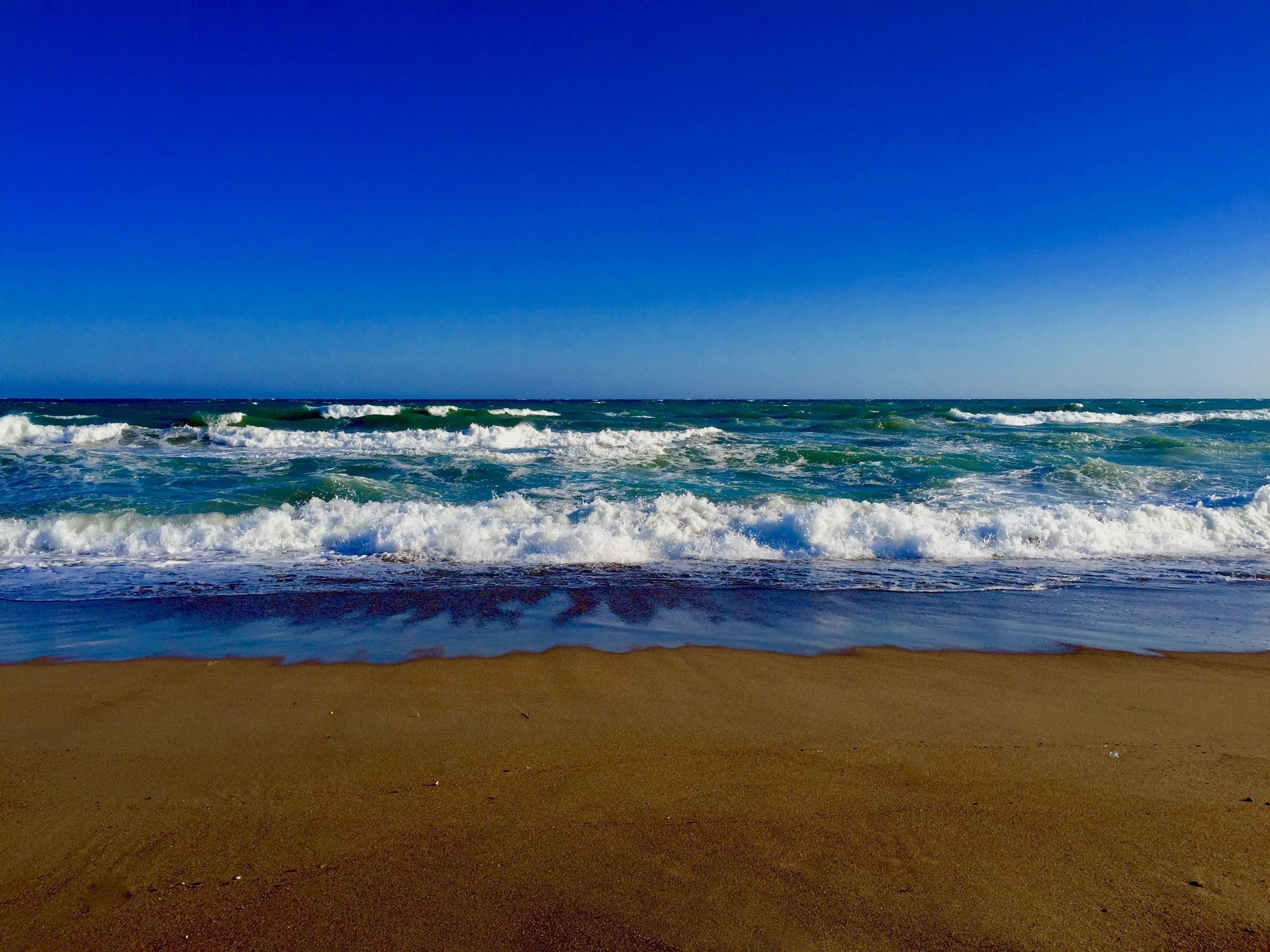 Una playa con olas rompiendo en la orilla bajo un cielo azul despejado.