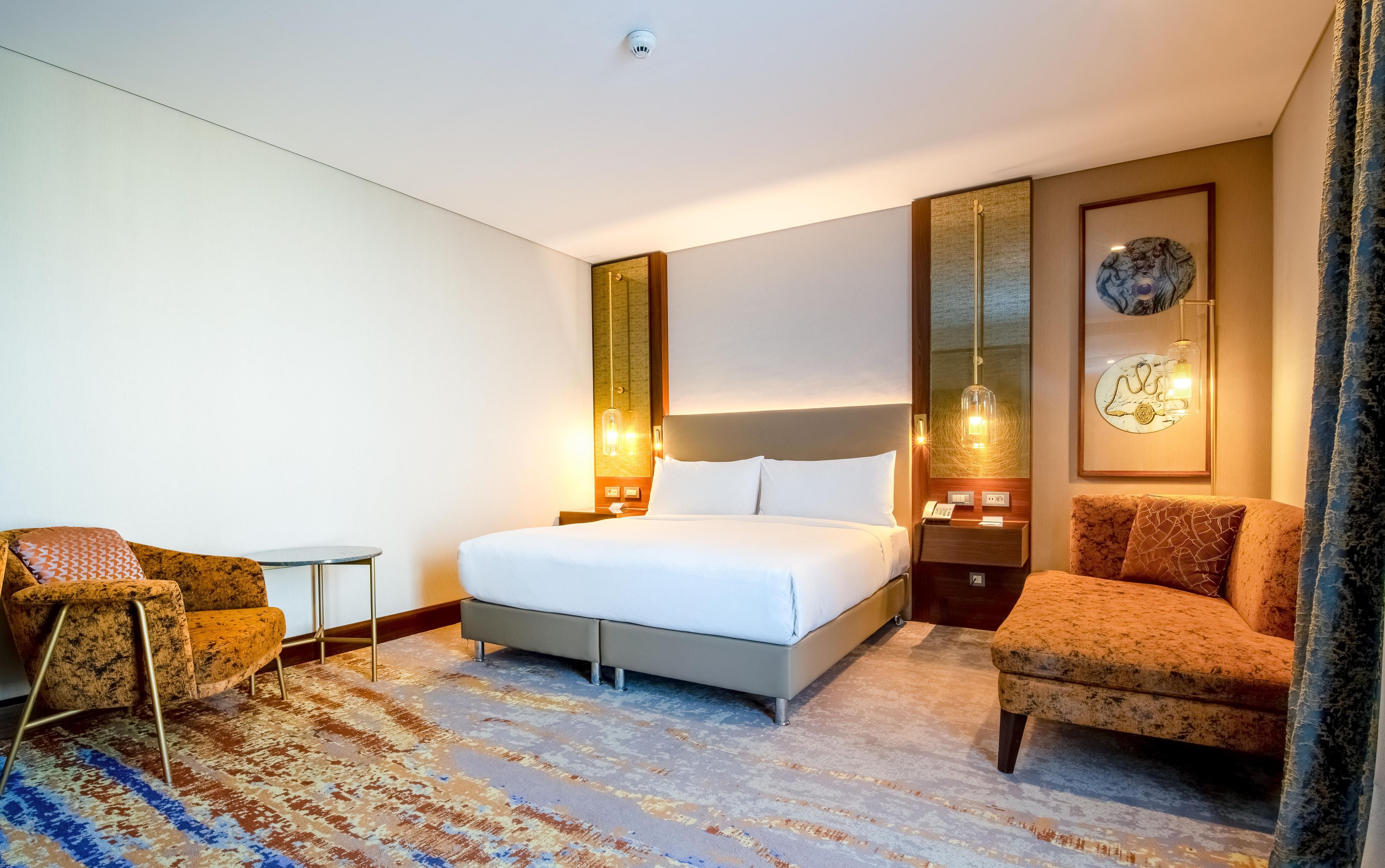A hotel room with a bed, two armchairs, a small table, and a decorative mirror.
