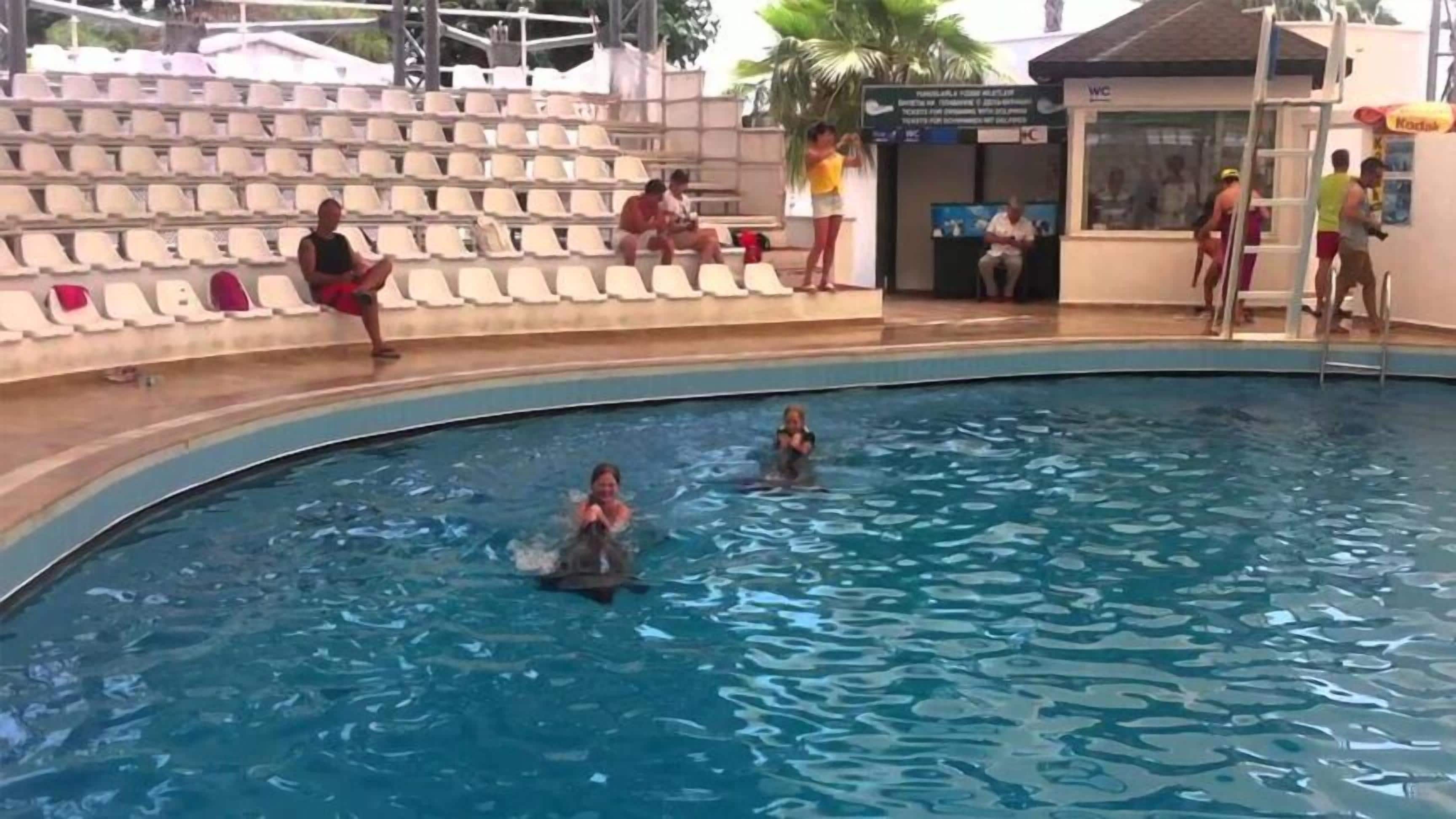 En swimmingpool med folk i vandet og andre på terrassen.