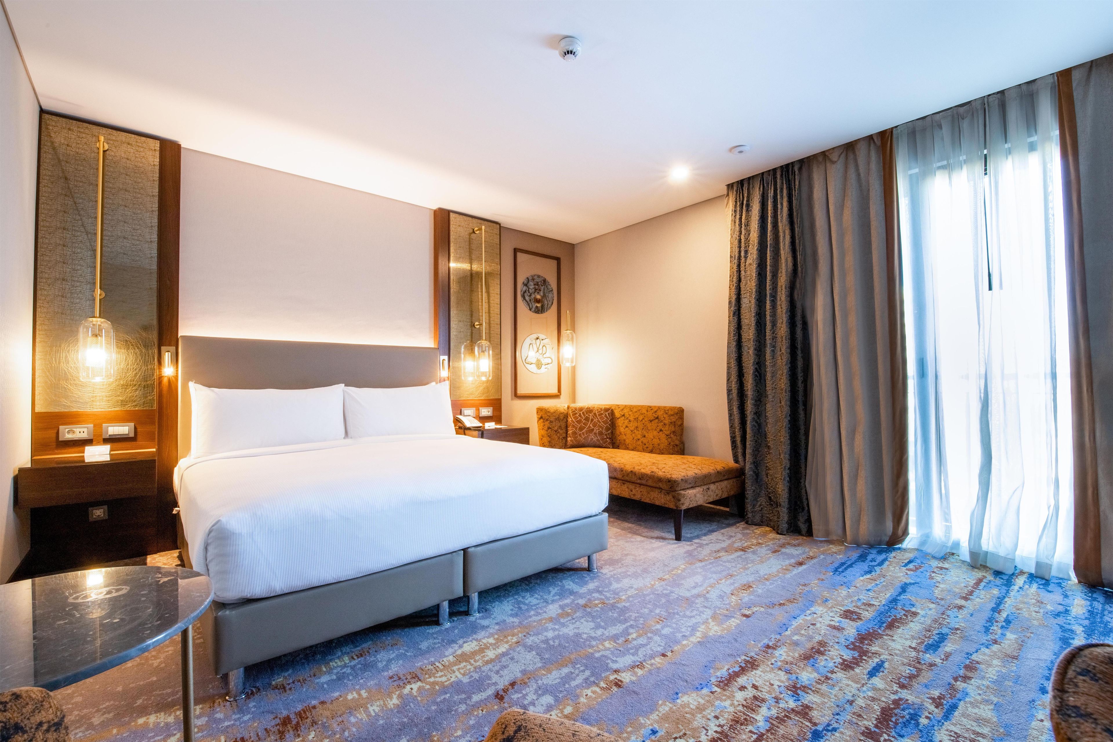 Une chambre d’hôtel dotée d’un grand lit, d’un coin salon, d’un bureau et offrant une vue sur l’extérieur.