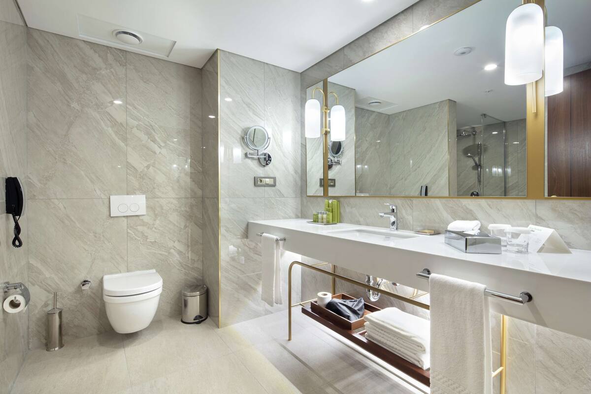 A modern bathroom with a marble wall, a large mirror, a toilet, a sink, and a shower area.