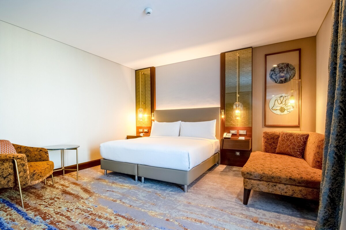 A hotel room with a bed, two armchairs, a small table, and a decorative mirror.