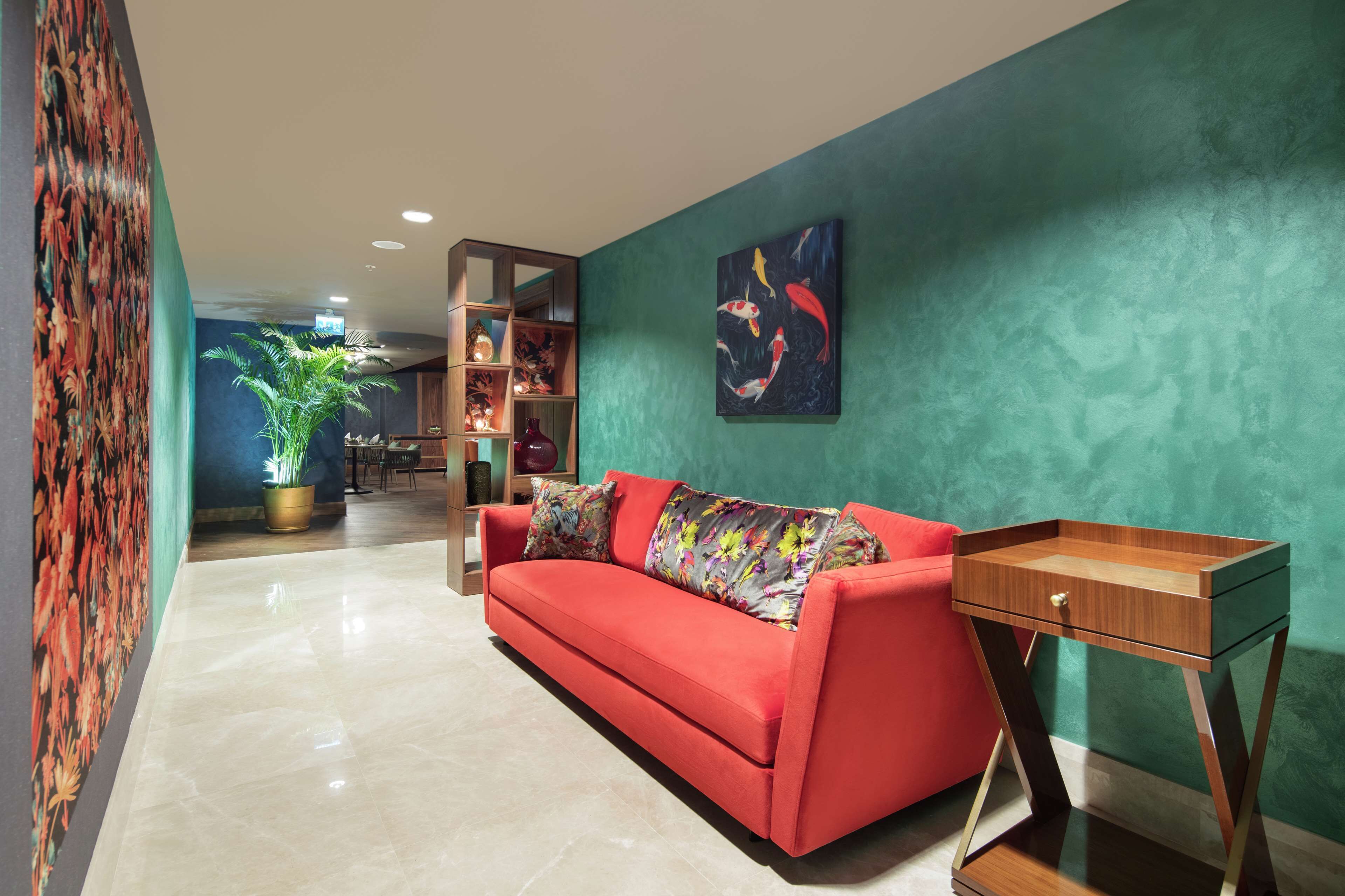 Un salon moderne avec un canapé rouge, une table d’appoint en bois, une plante en pot et un tableau coloré accroché au mur.