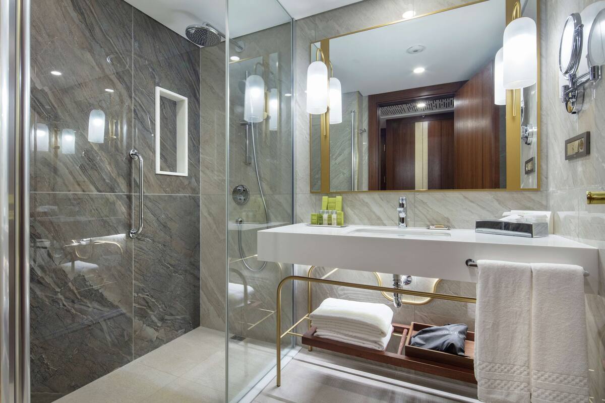 A modern bathroom with a glass-enclosed shower, a large mirror, and a vanity with a sink and towel rack.