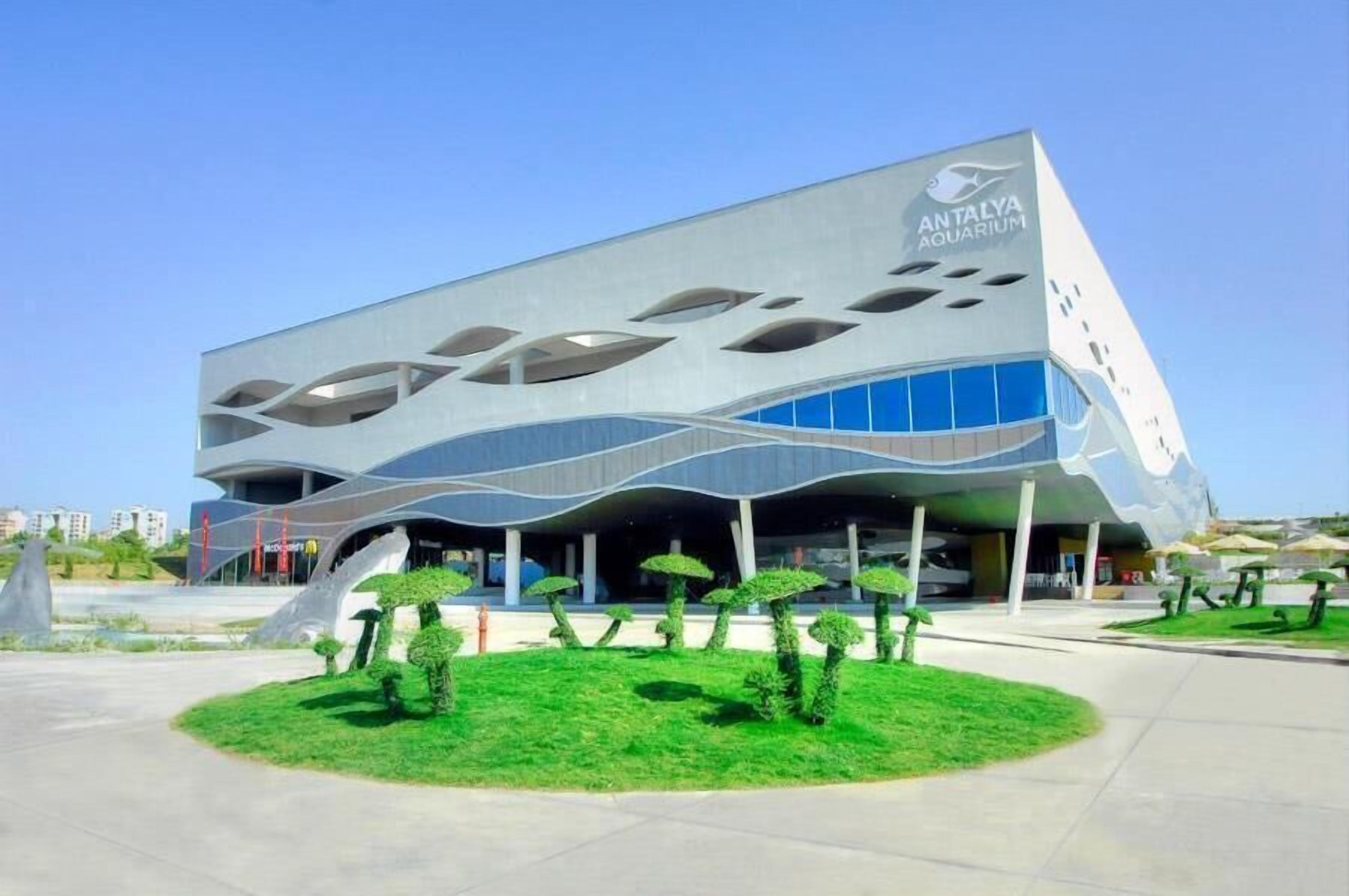A modern building with a unique wavy facade and the name "ANTALYA AQUARIUM" on the side.