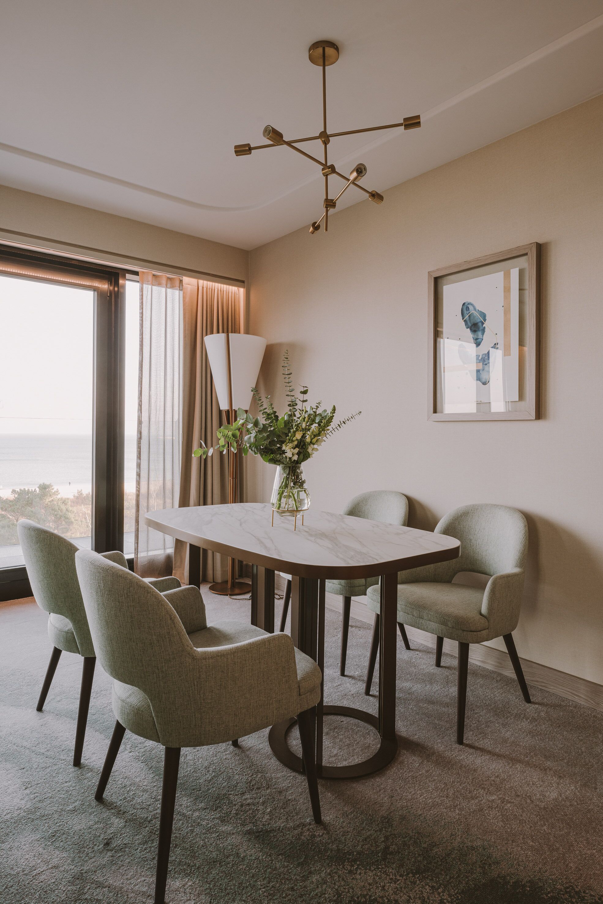 Un'area pranzo moderna con un tavolo rotondo, quattro sedie, un vaso con fiori, una lampada da terra e una lampada a sospensione.