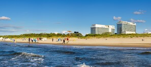 Un hotel sulla spiaggia con diversi piani, una spiaggia sabbiosa e un’area dunosa erbosa.