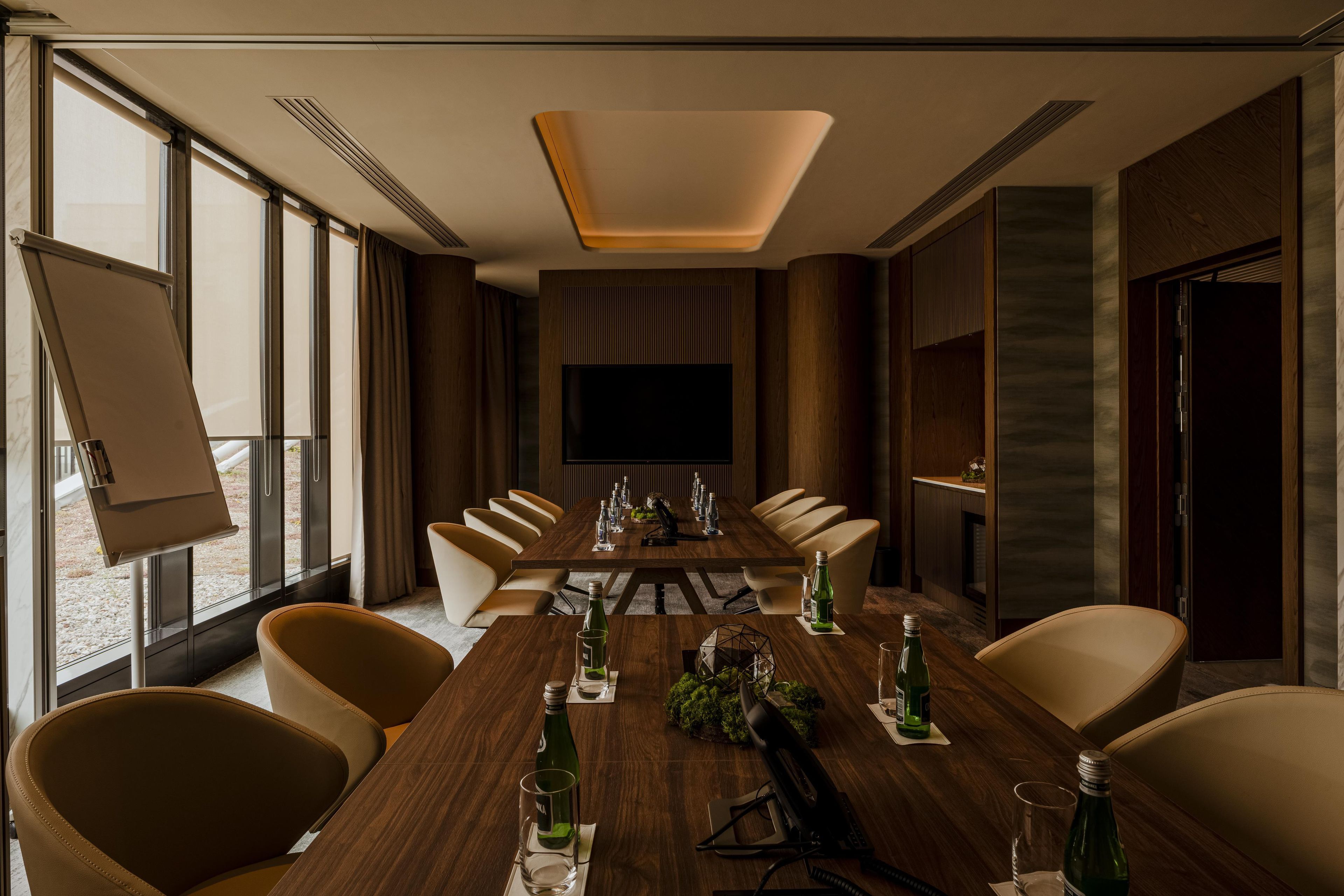 A conference room with a long table, chairs, a projector screen, and a large window.