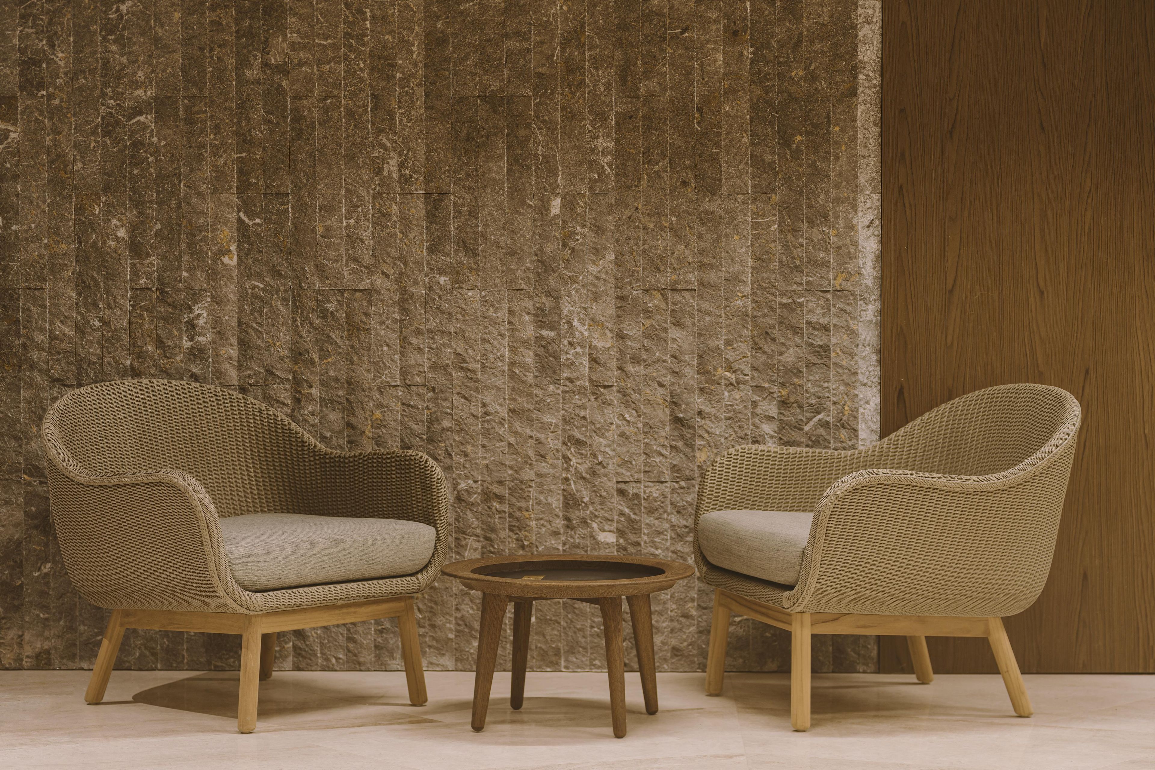 Two wicker chairs with cushions and a small wooden table in front, against a textured wall.