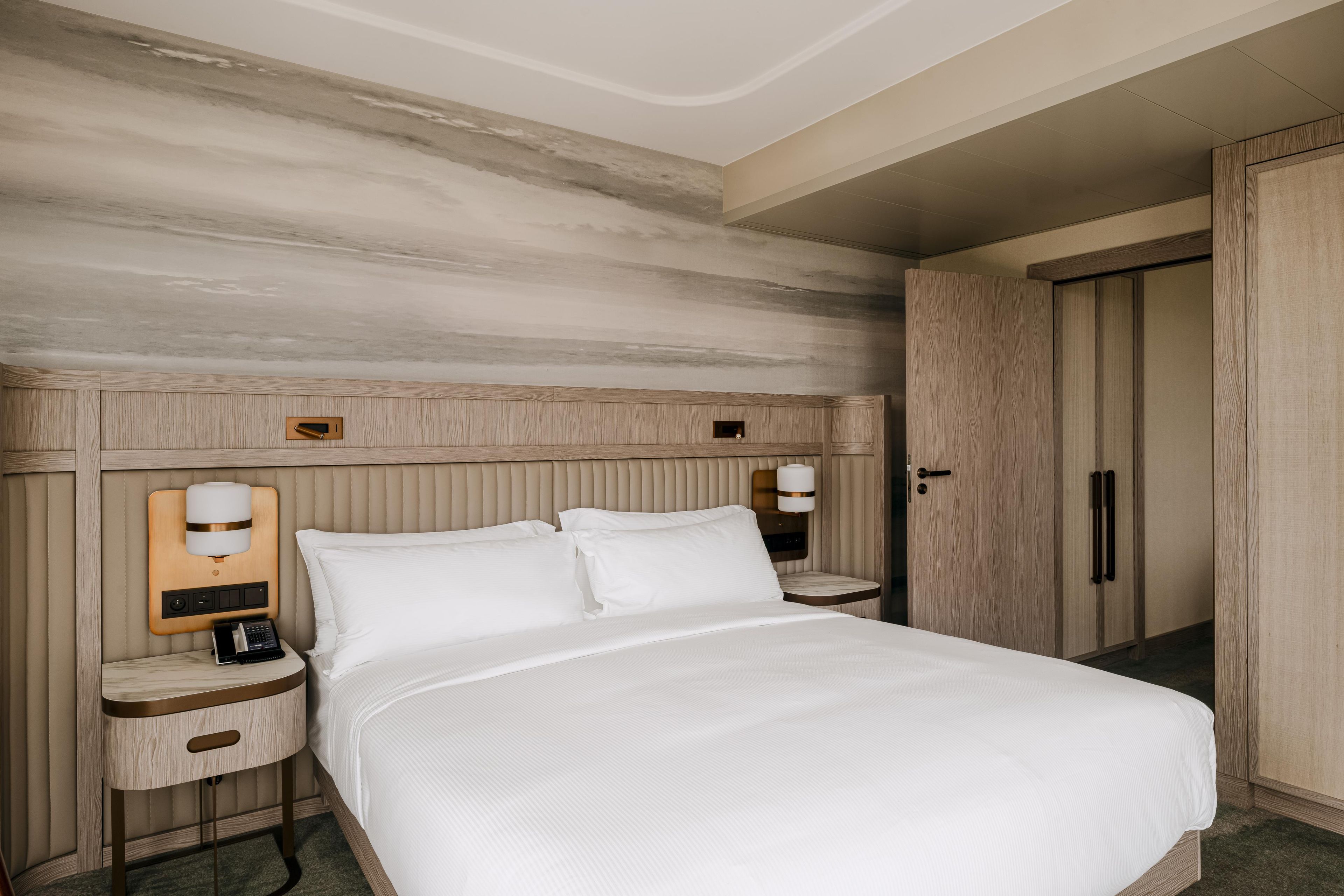 Habitación de hotel con una cama grande, mesitas de noche, un armario y una lámpara de pared.