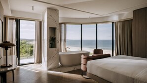 Una habitación de hotel moderna con una cama grande, una bañera y vistas al océano.