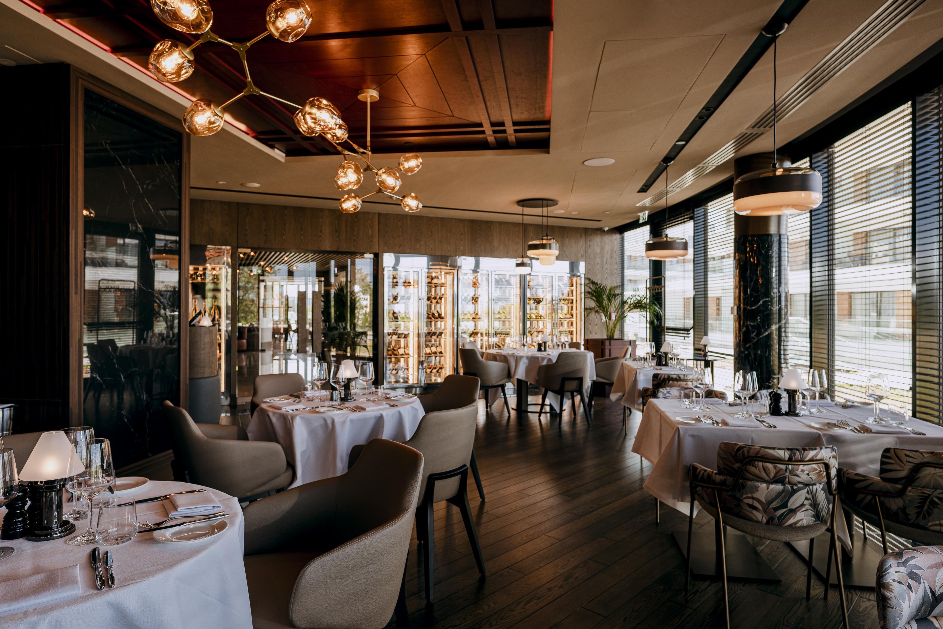 Ein Restaurantinneres mit runden Tischen, Stühlen und einer modernen Kronleuchter.