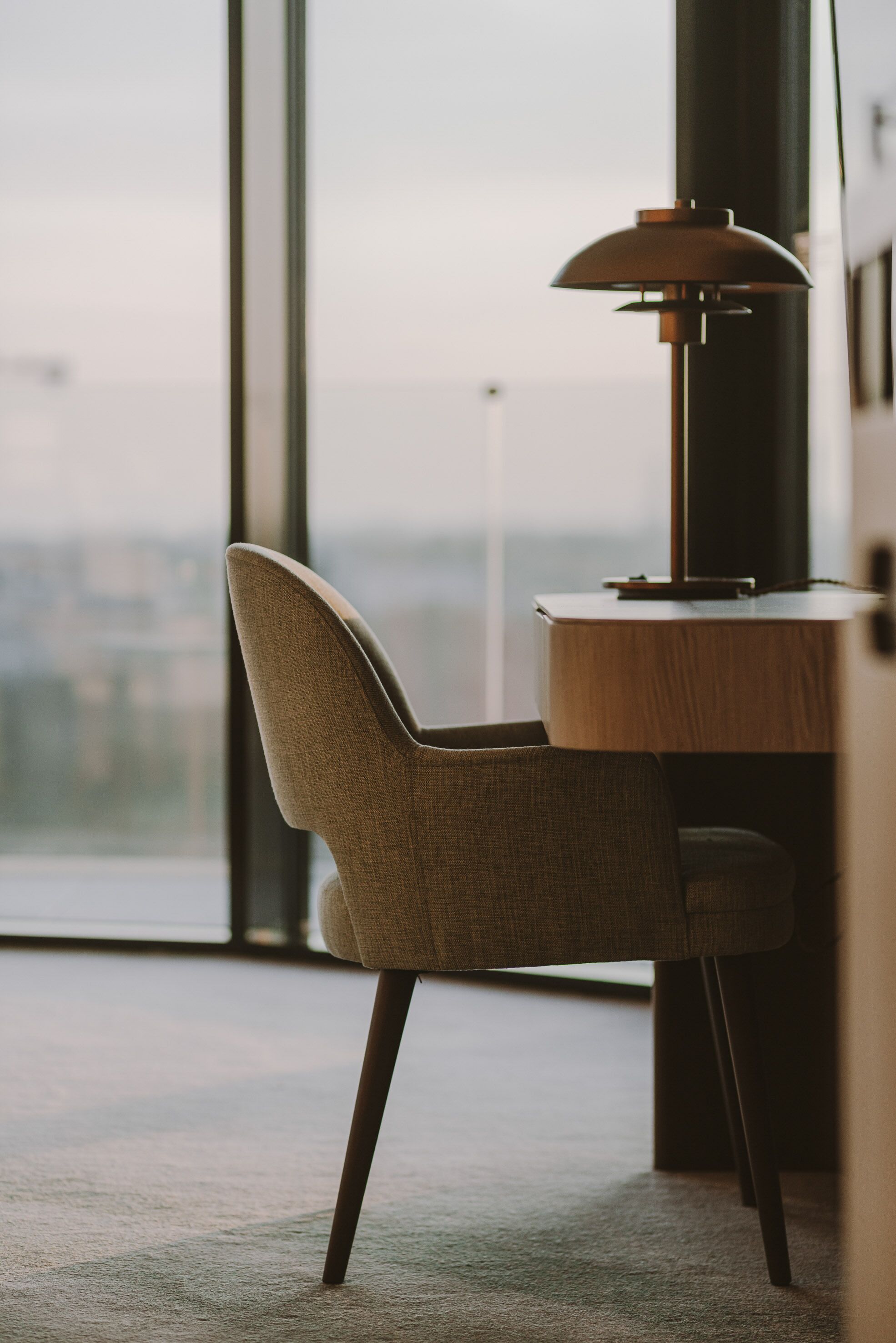 A modern office chair with a high backrest and a wooden desk with a lamp.
