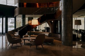 Een moderne lobby met een gebogen trap, lederen zitplaatsen en een grote vloerlamp.