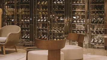 Una bodega con estantes llenos de botellas de vino, dos sillones tapizados y una mesa de centro de madera.