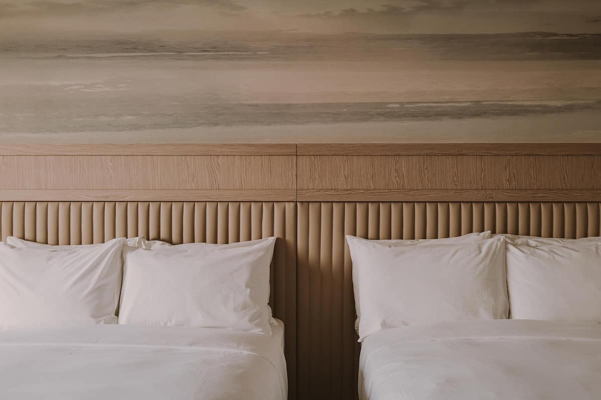 Habitación de hotel con cabecera, dos camas y vista al cielo.