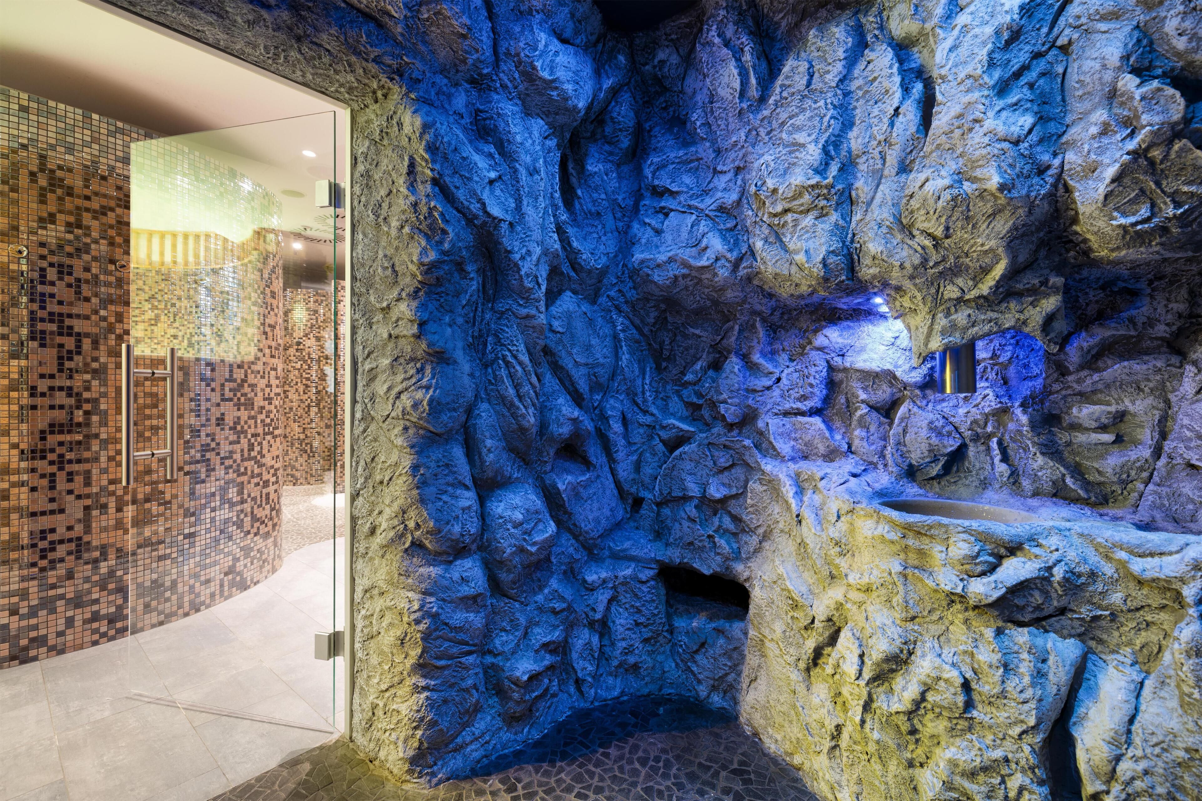 A bathroom with a mosaic tile wall, a glass shower enclosure, and a stone wall feature.