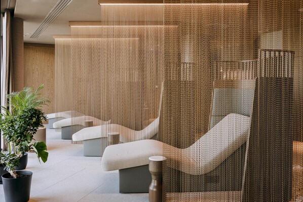 A modern waiting area with cushioned seating, a potted plant, and a textured partition.