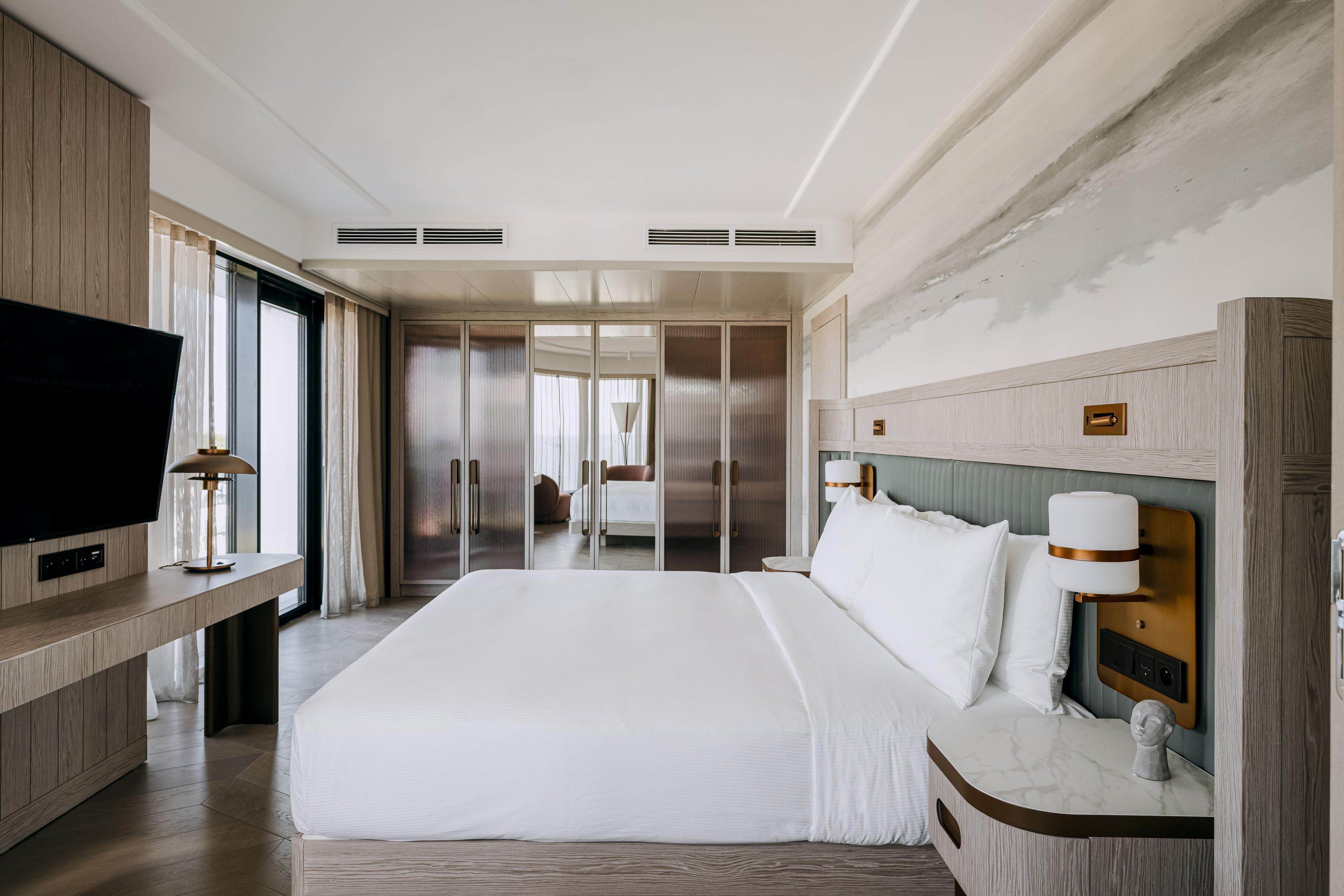 A hotel room with a large bed, a TV, a bedside table, and a wardrobe.