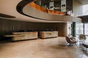 Een moderne lobby met een gebogen receptiebalie, een zithoek en een trap naar een hoger niveau.
