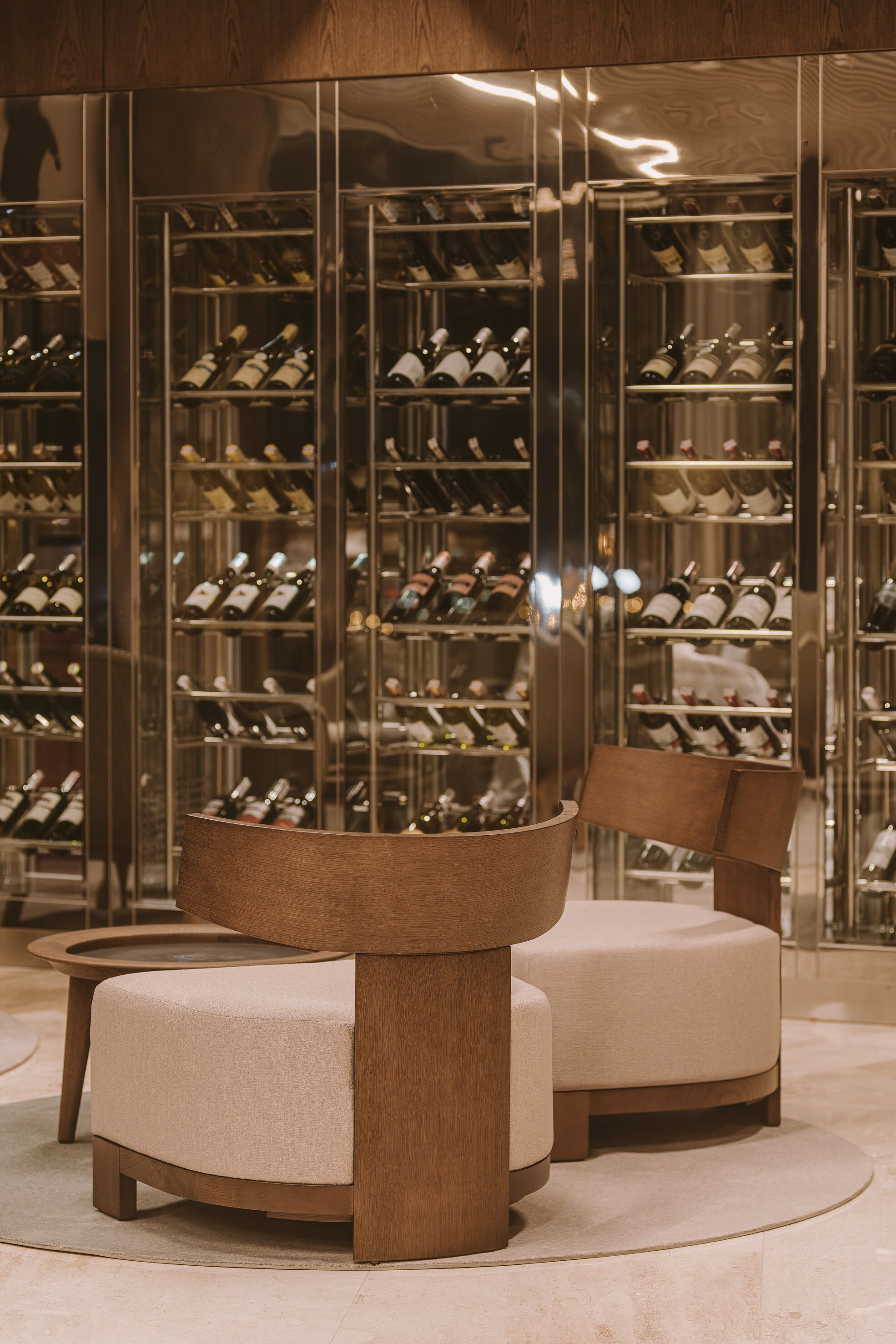 A modern interior with a wine cellar, two wooden chairs, and a marble floor.