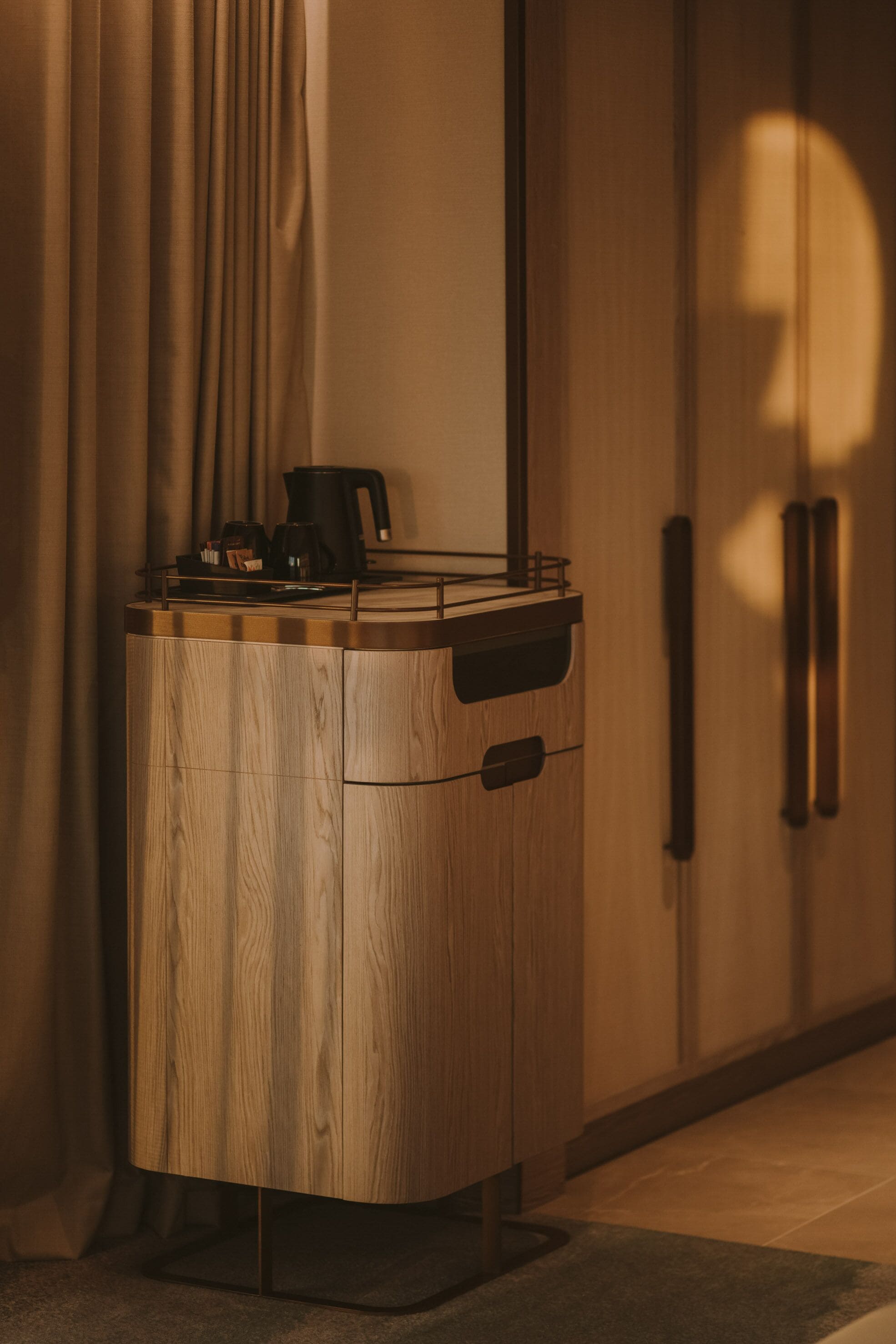 A wooden cabinet with a coffee maker on top, positioned against a wall with a curtain.