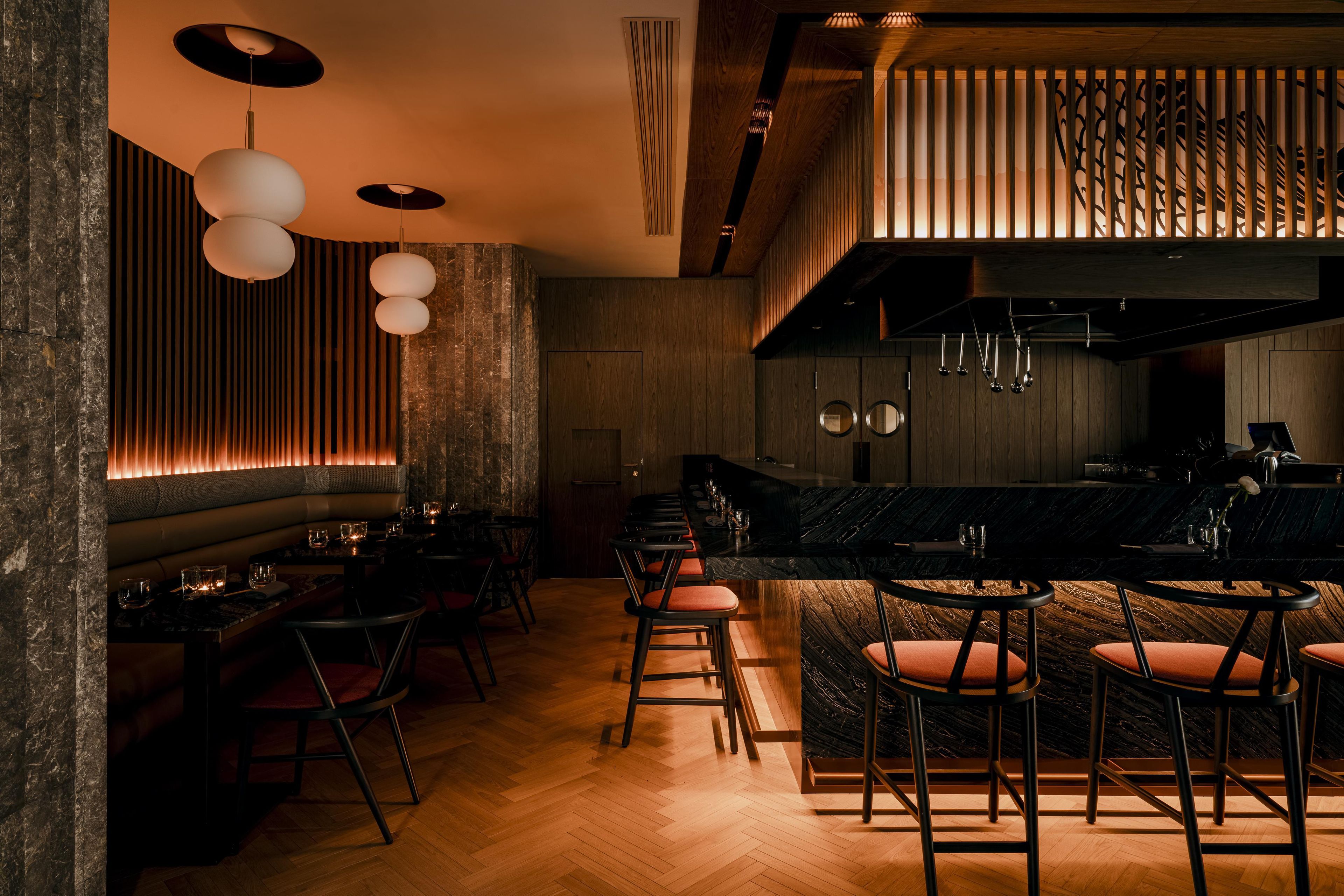 A modern bar area with wooden accents, a marble countertop, and a seating arrangement with bar stools.