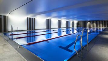 Une piscine intérieure moderne, dotée de plusieurs couloirs de nage, d’une eau claire et de rampes en métal.