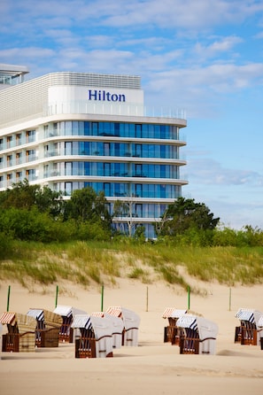 Ein mehrstöckiges Hotel mit einem gut sichtbaren "Hilton"-Schild, umgeben von Liegestühlen und Dünen.