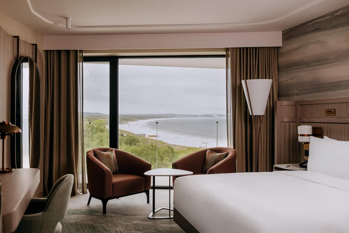 Habitación de hotel con una cama grande, dos sillones, una mesita y vistas a la playa.