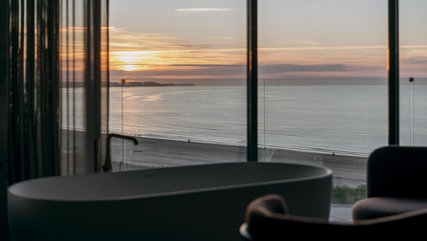 Una habitación con un ventanal grande que da a una playa al atardecer.