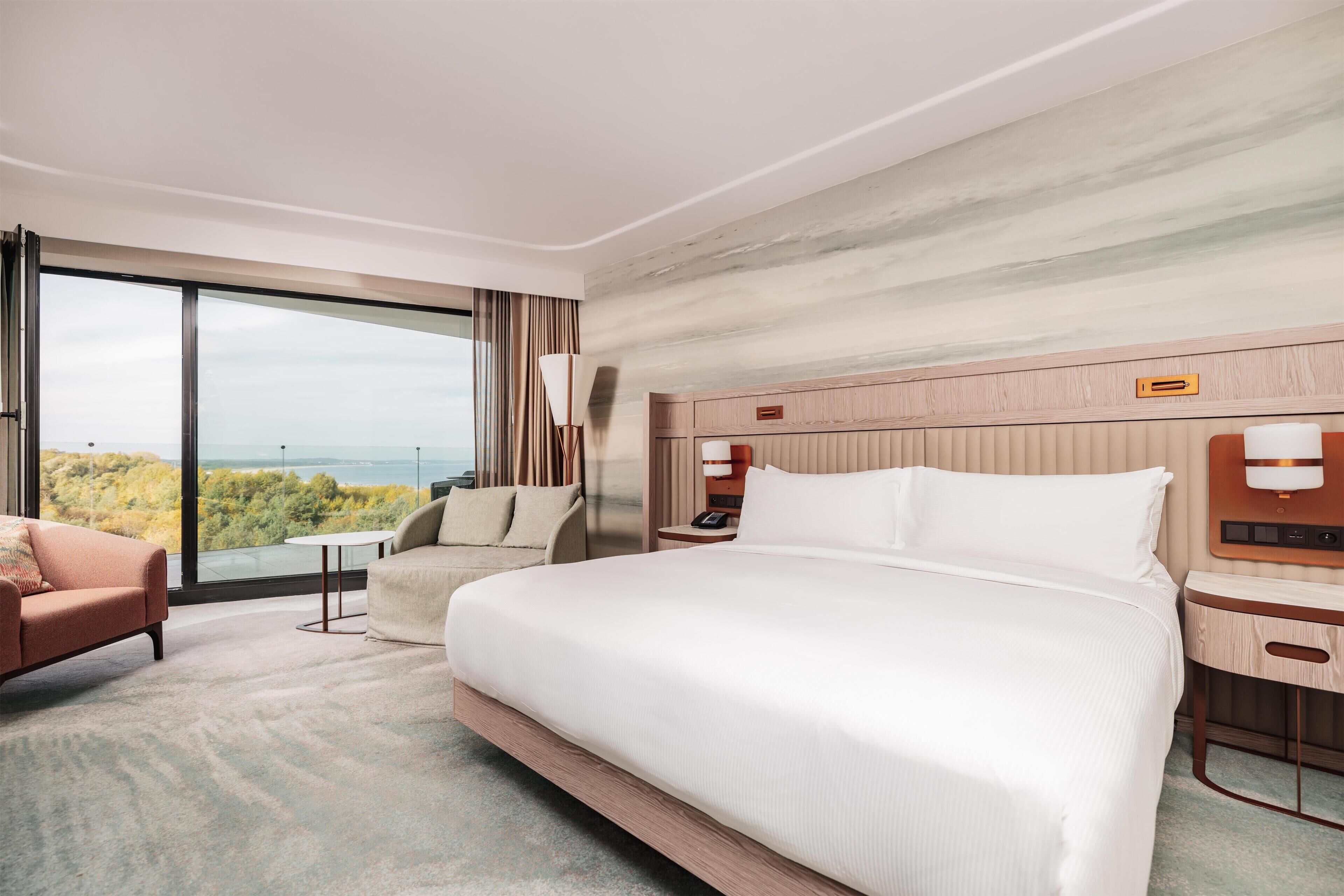Una habitación de hotel con una cama grande, un escritorio, una silla y vistas al exterior.