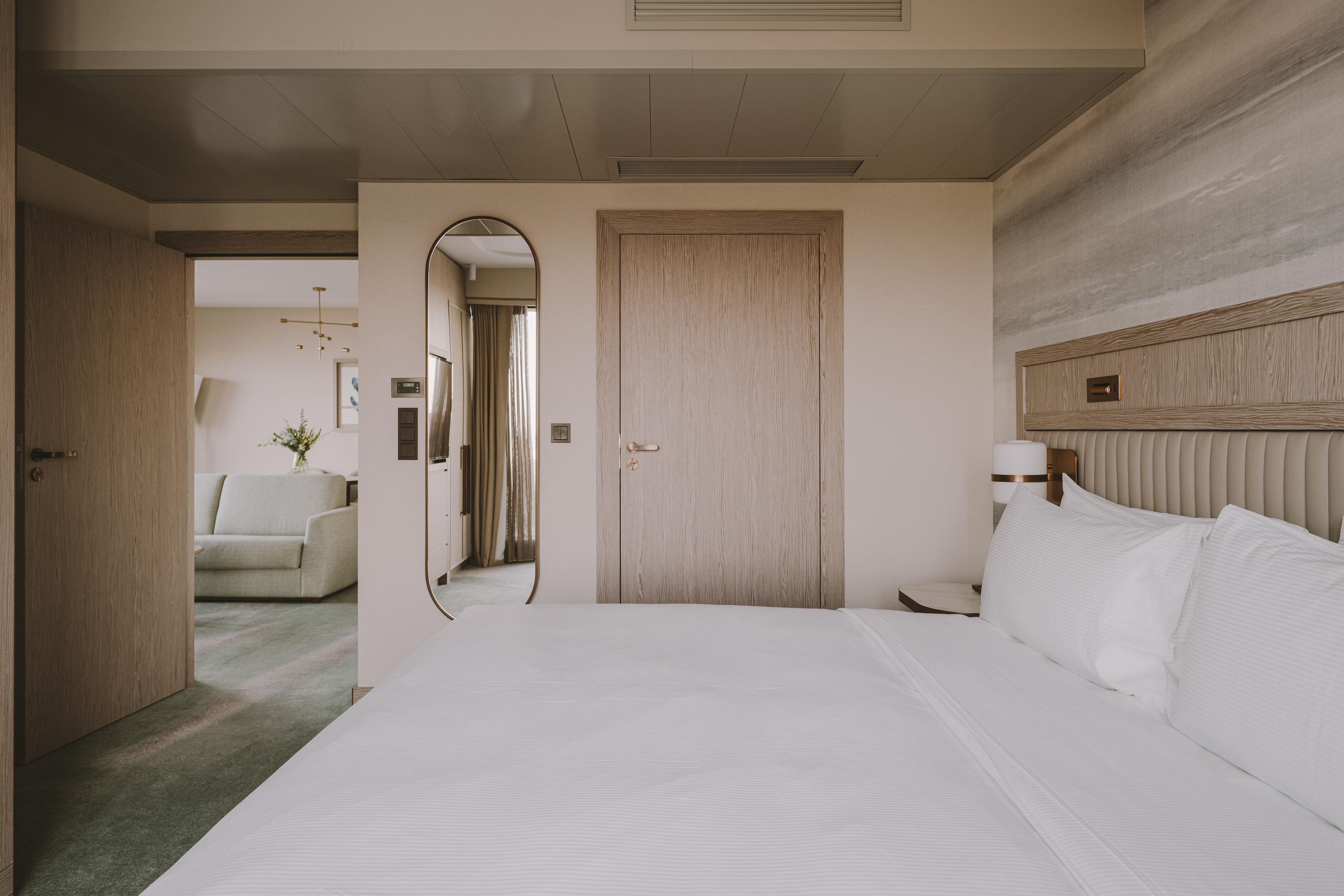 A hotel room with a large bed, a wooden headboard, a mirror, and a door leading to a bathroom.