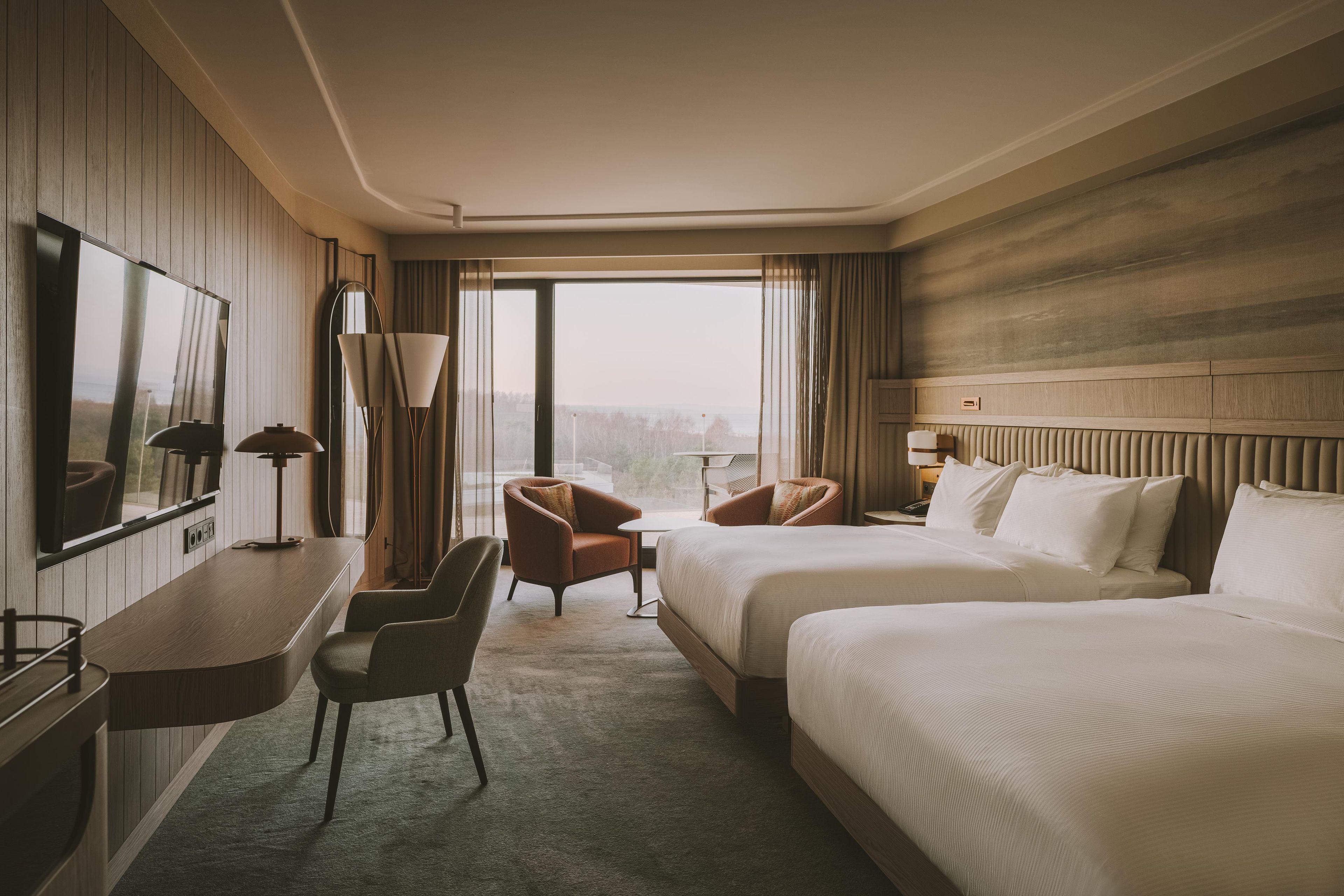 Quarto de hotel com uma cama grande, escrivaninha, cadeira e vista para o exterior.