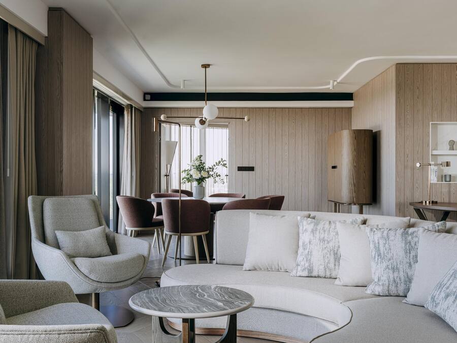 A modern living room with a sofa, armchairs, a coffee table, and a dining area with chairs and a table.