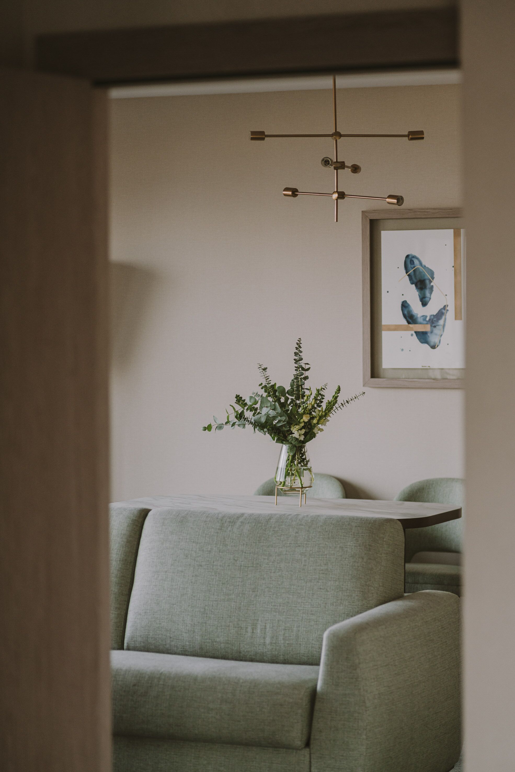 A room with a modern chandelier, a framed artwork on the wall, and a vase with greenery on a table.