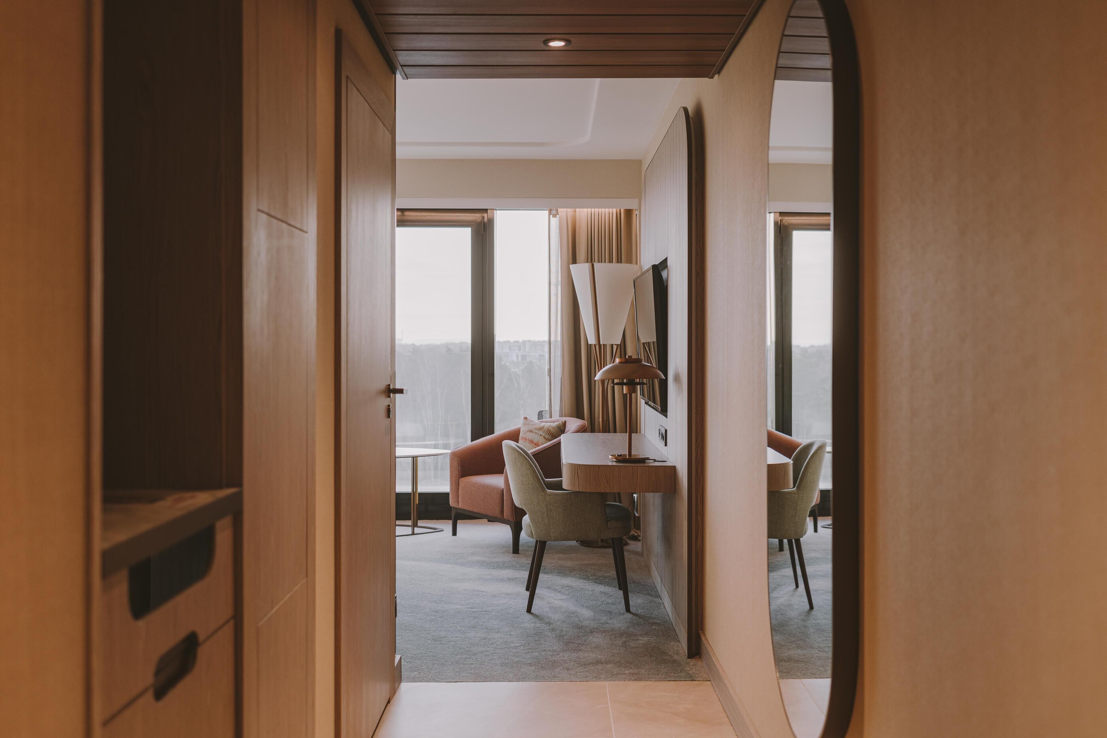 A hotel room with a view, a desk, a chair, and a lamp.