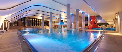 An indoor swimming pool with a modern design, featuring a large pool area, lounge chairs, and a unique red sculpture.