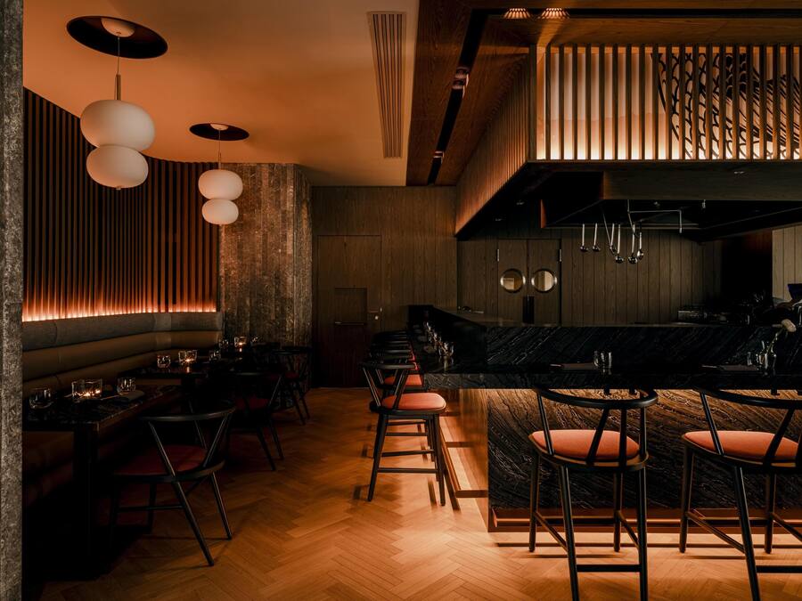 Un área de bar moderna con paneles de madera, una encimera de mármol y varias lámparas colgantes.