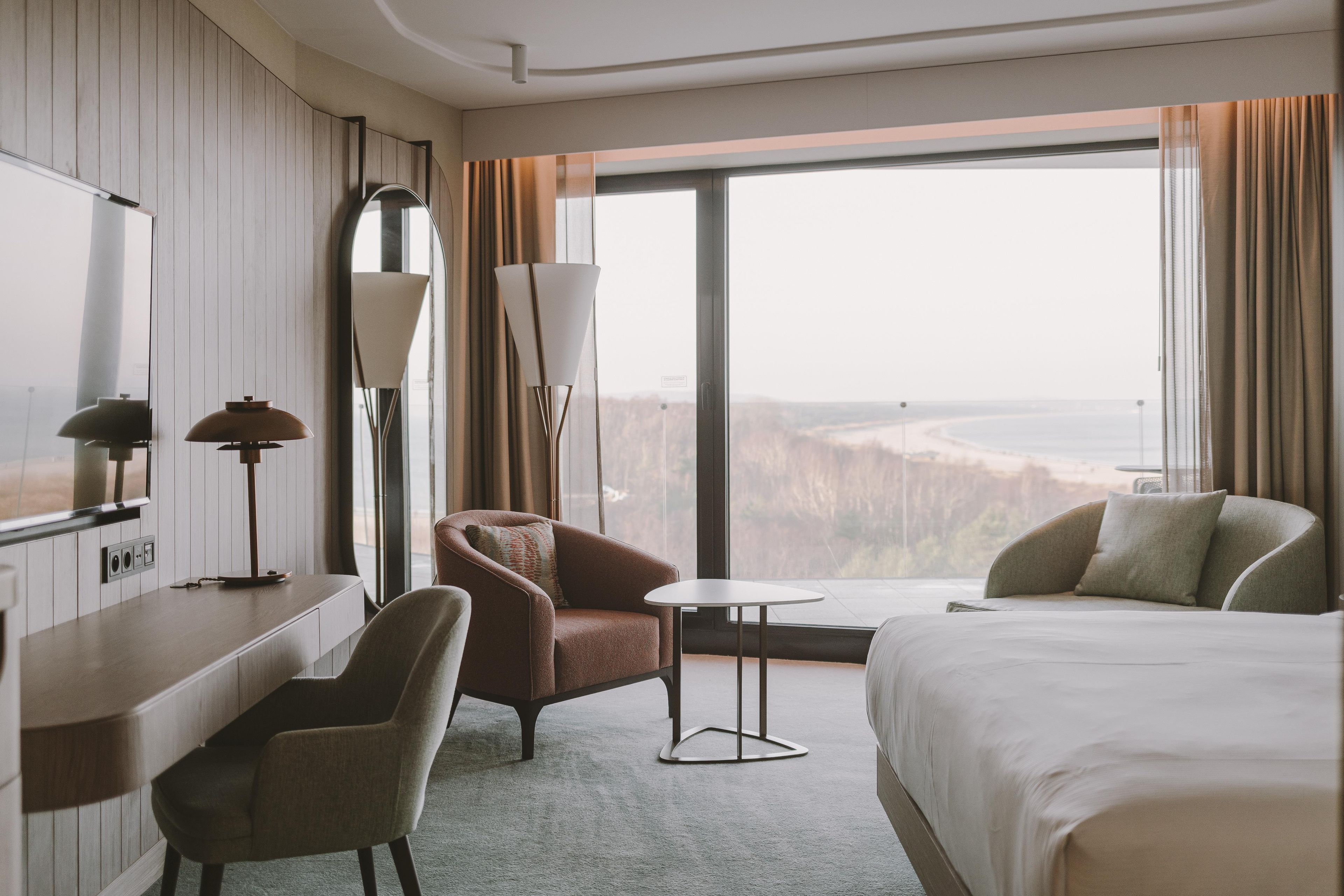 Una camera d'albergo con un letto, una scrivania, una sedia, una lampada e vista sul paesaggio.