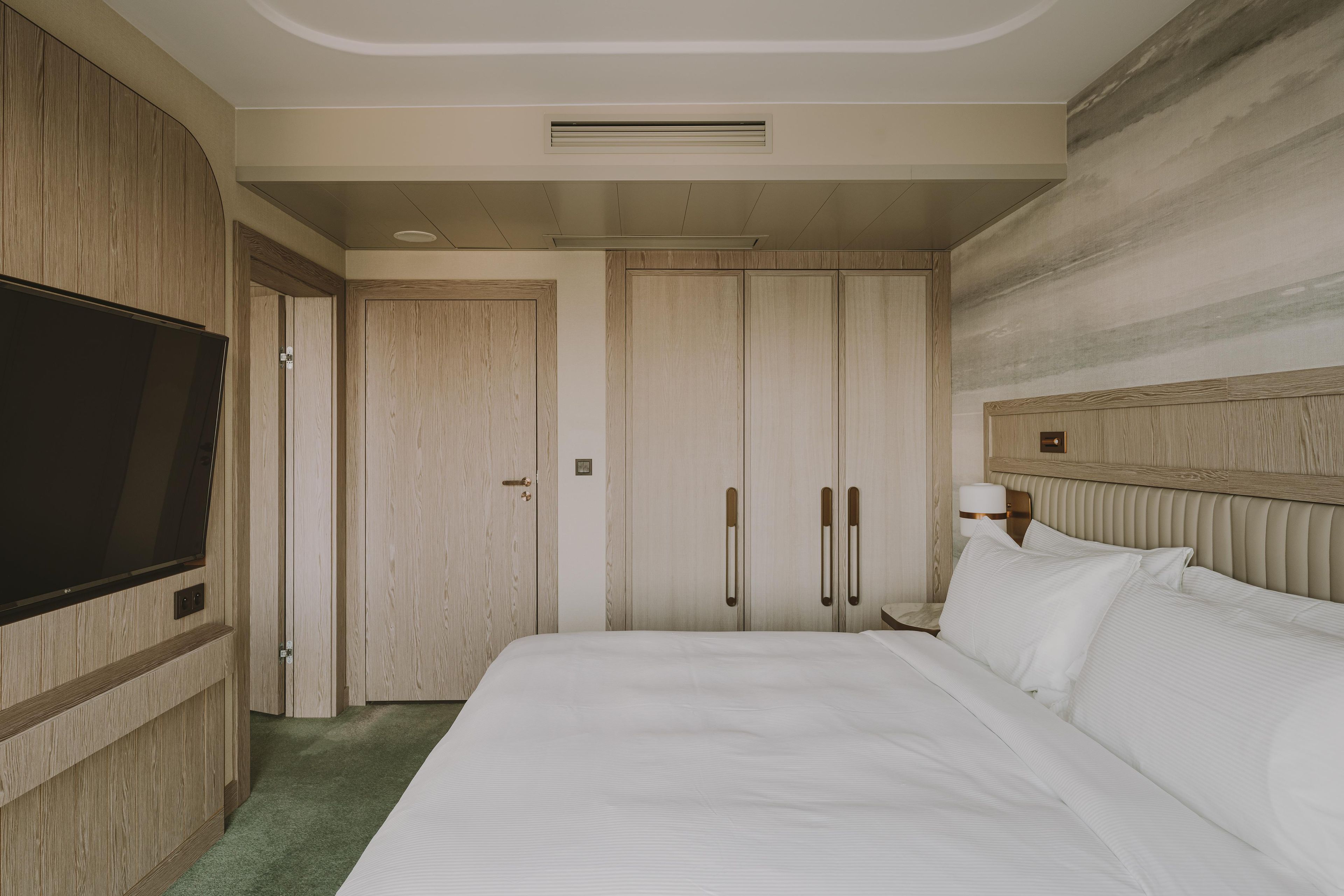 Una habitación de hotel con una cama grande, televisión, armario y mesita de noche con lámpara.