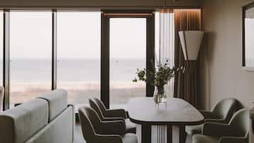 A modern dining area with a large table, chairs, a vase with flowers, and a view of the ocean.
