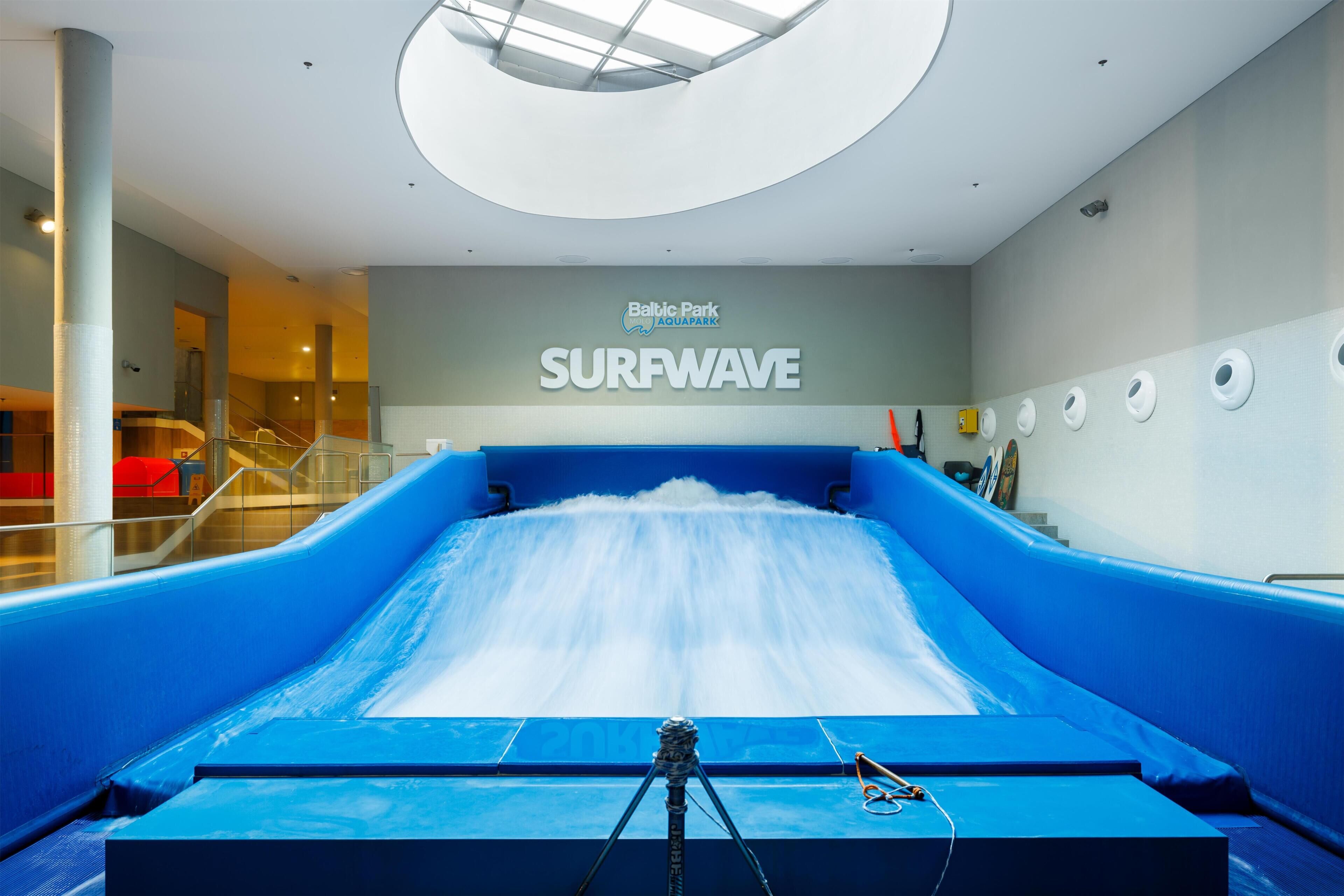 Un tobogán de agua grande en el interior con un letrero que dice 'SURF WAVE', un tragaluz y vistas de una escalera.