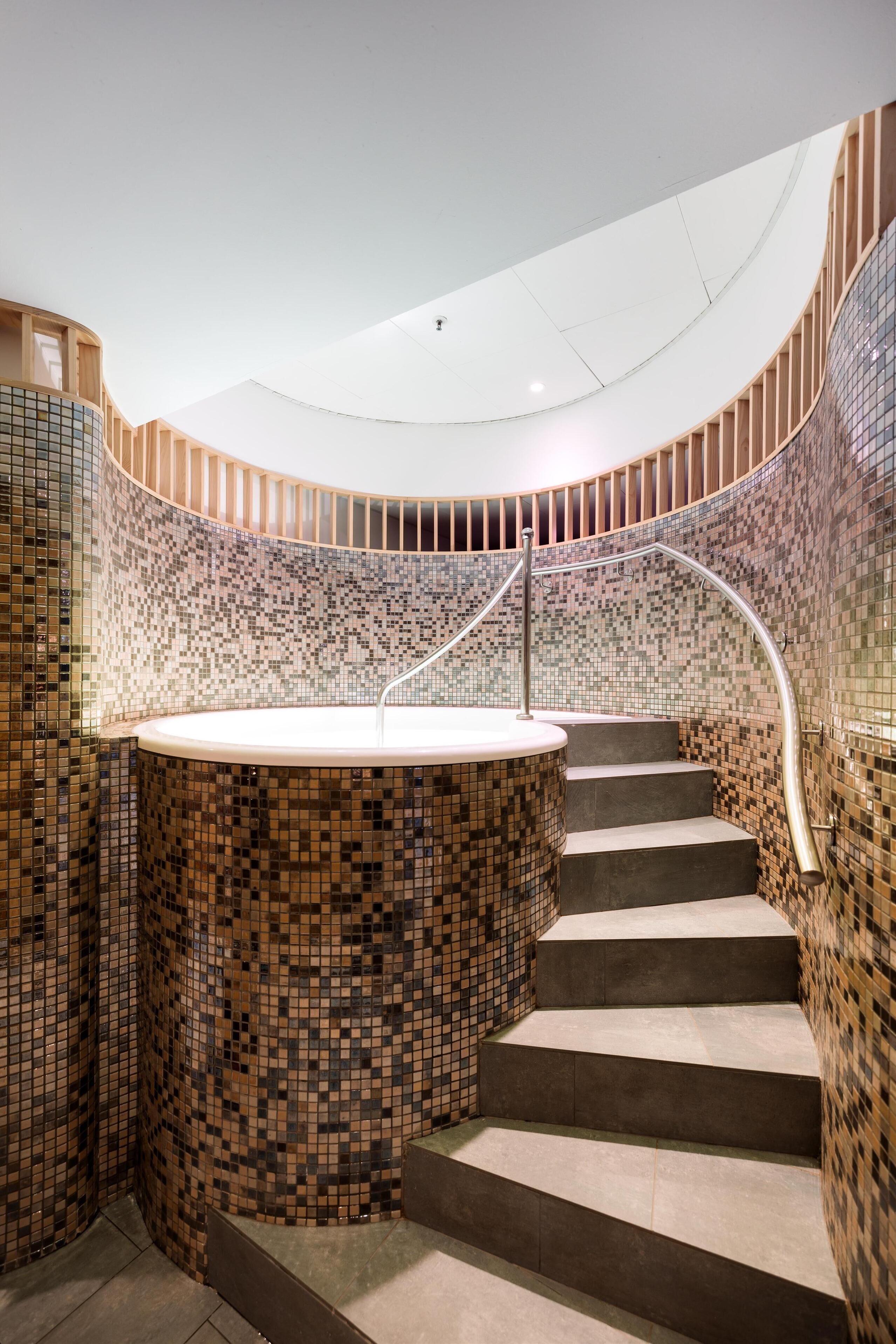 A curved staircase with a mosaic-tiled wall and a central circular feature, possibly a hot tub or fountain.
