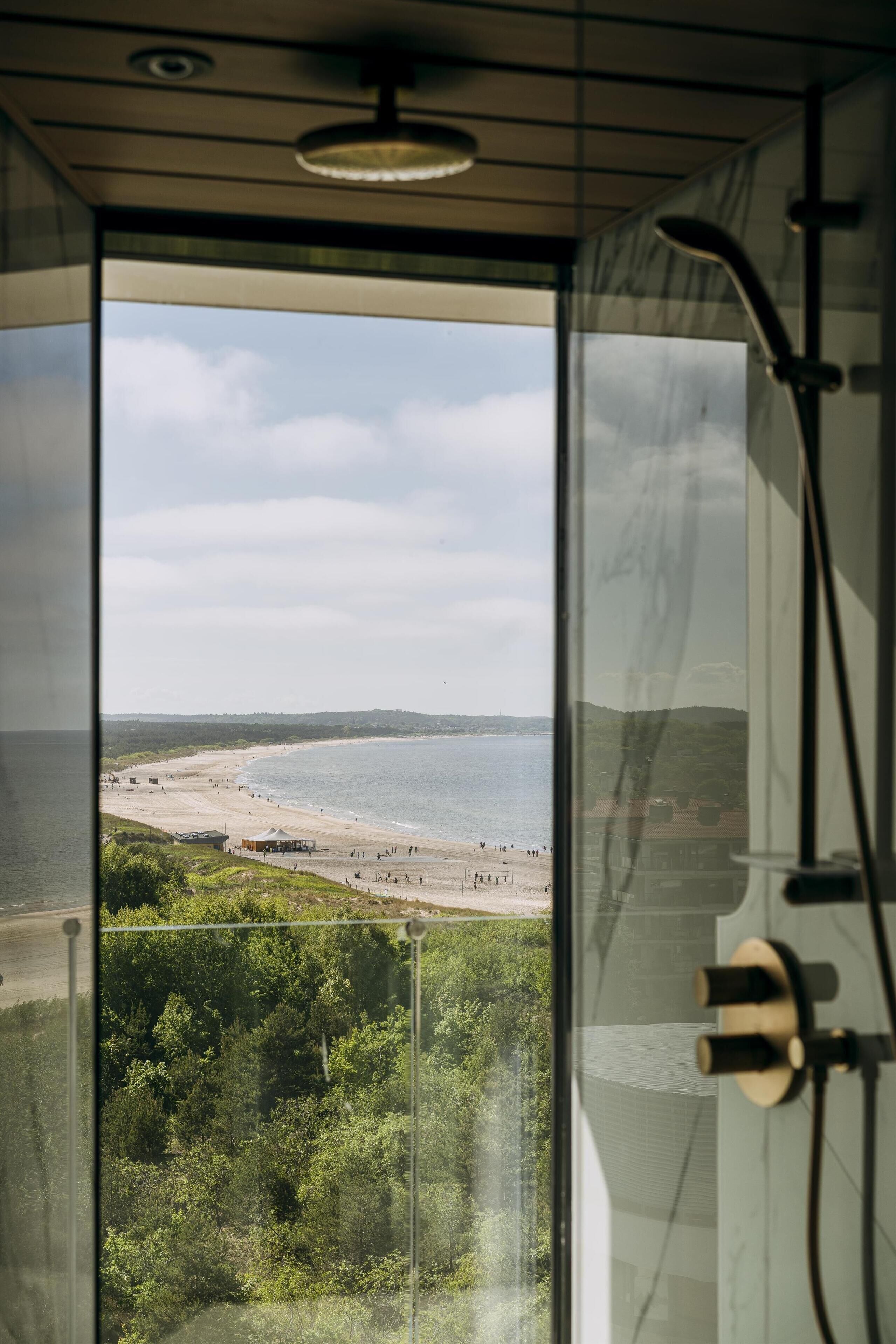 A room with a large window overlooking a beach and forested area.