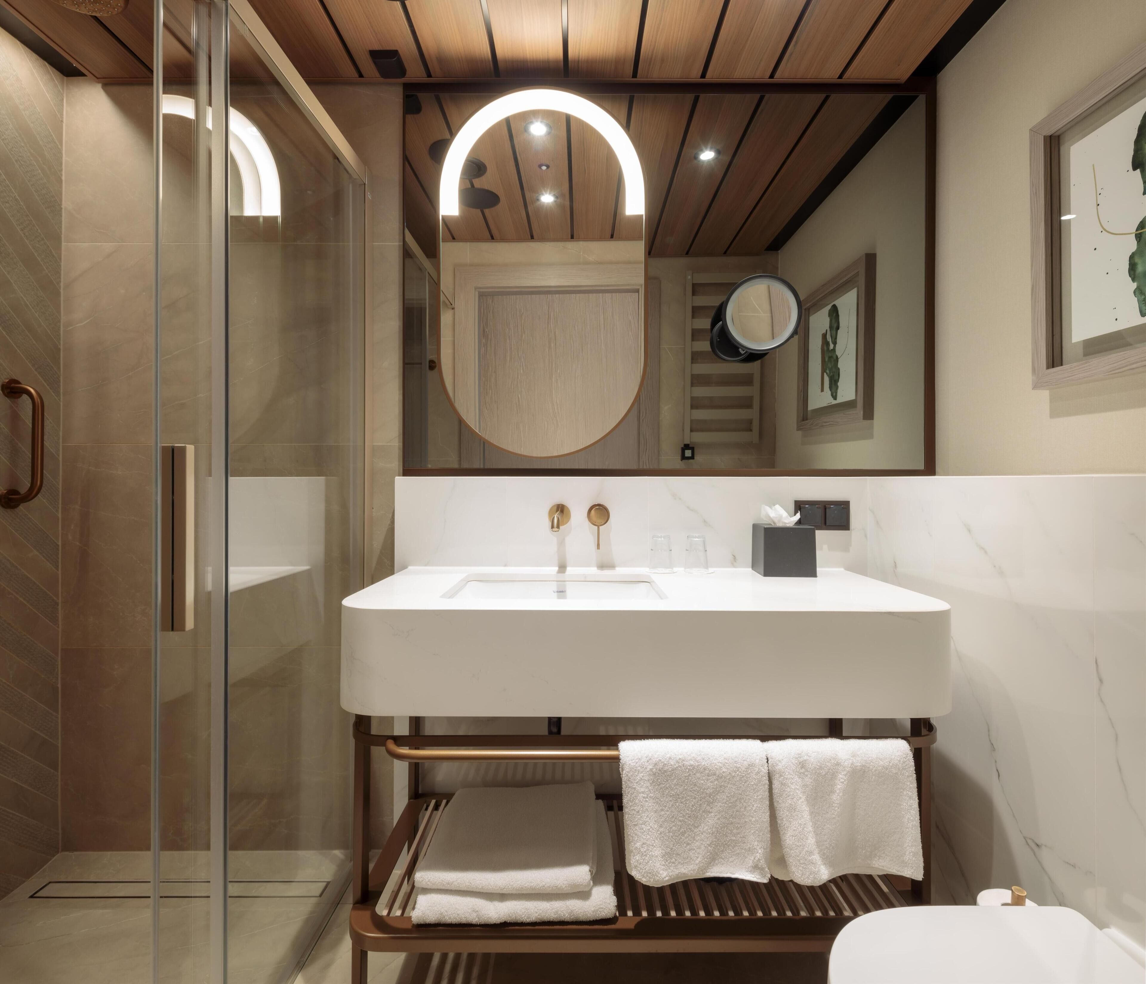 A modern bathroom with a glass shower enclosure, a wooden vanity with a white sink, and a large mirror above the sink.