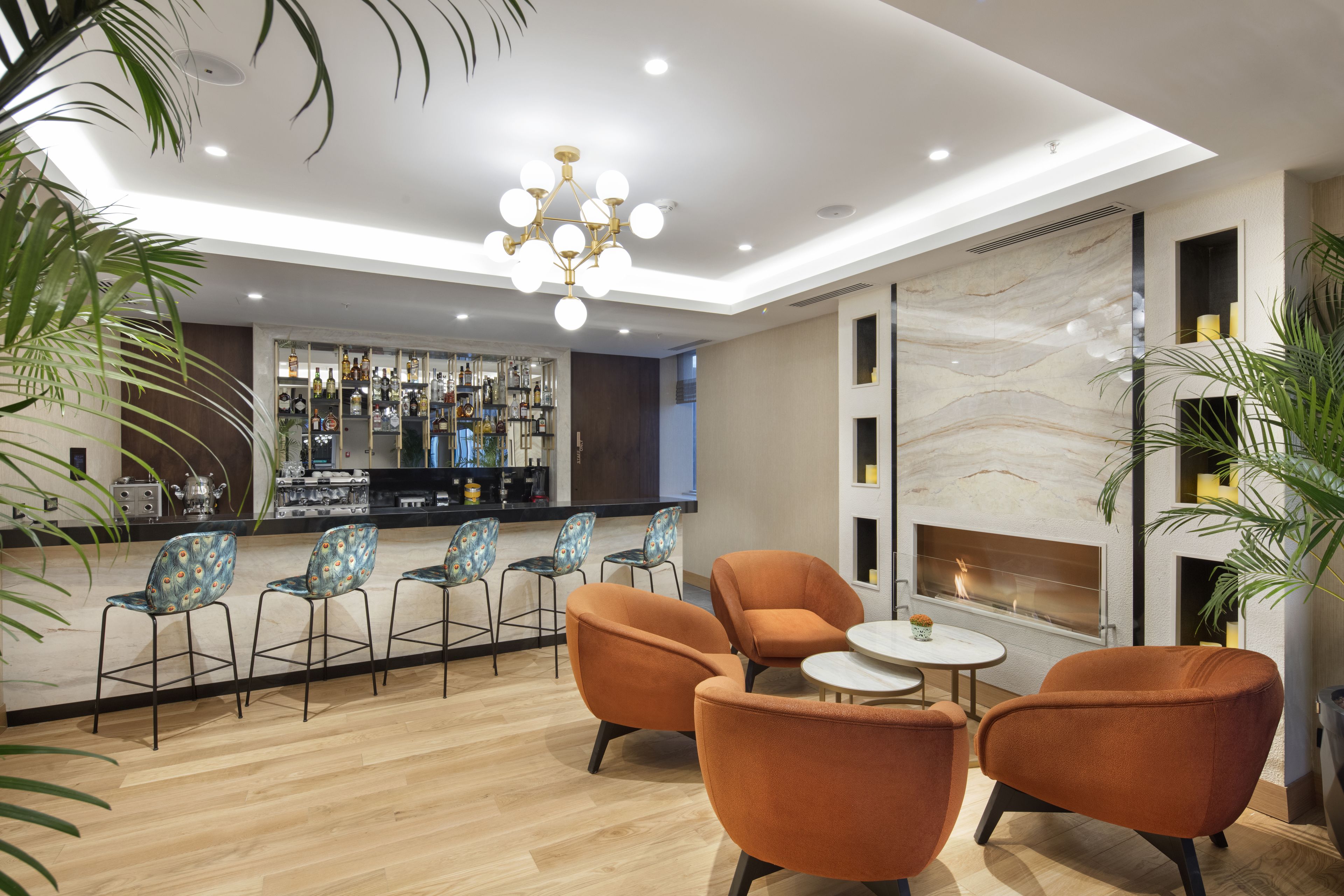 A modern bar area with a marble wall, a fireplace, and orange chairs.