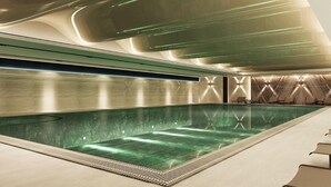 Una piscina interior moderna de color verdoso, con un largo banco a un lado y un diseño de pared con motivos.