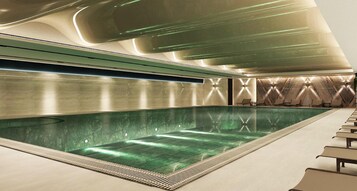 Una piscina interior moderna de color verdoso, con un largo banco a un lado y un diseño de pared con motivos.