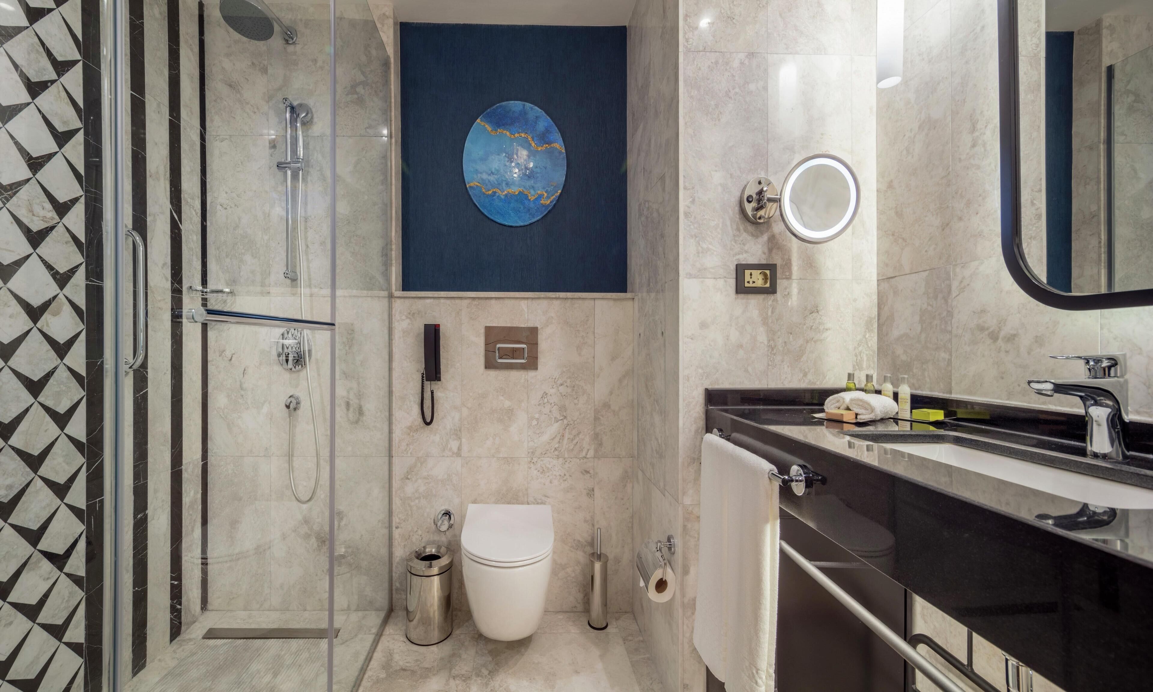 Un baño moderno con ducha de vidrio, inodoro, lavabo con espejo y teléfono en la pared.